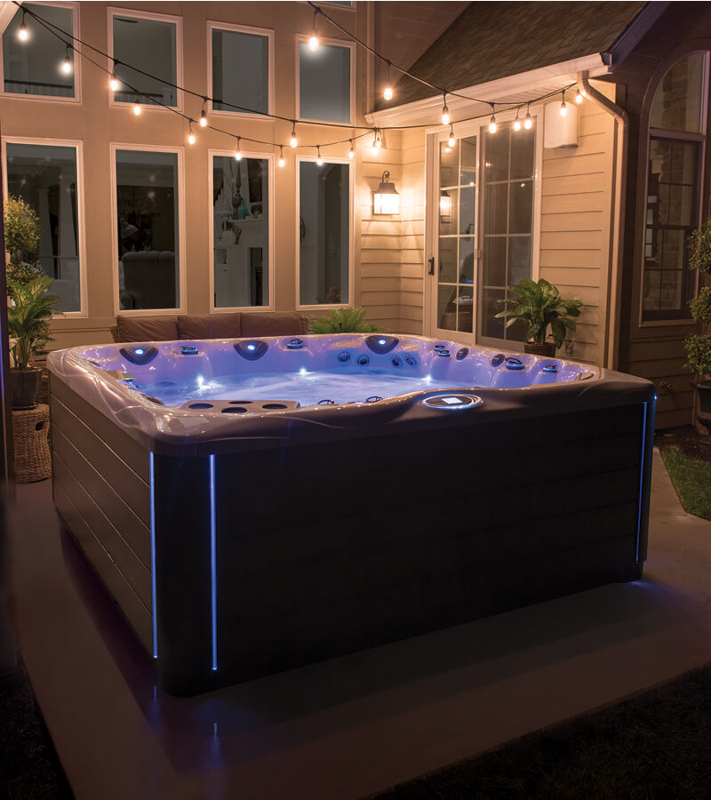 A Master Spas hot tub with blue lighting on a patio beside a house at night