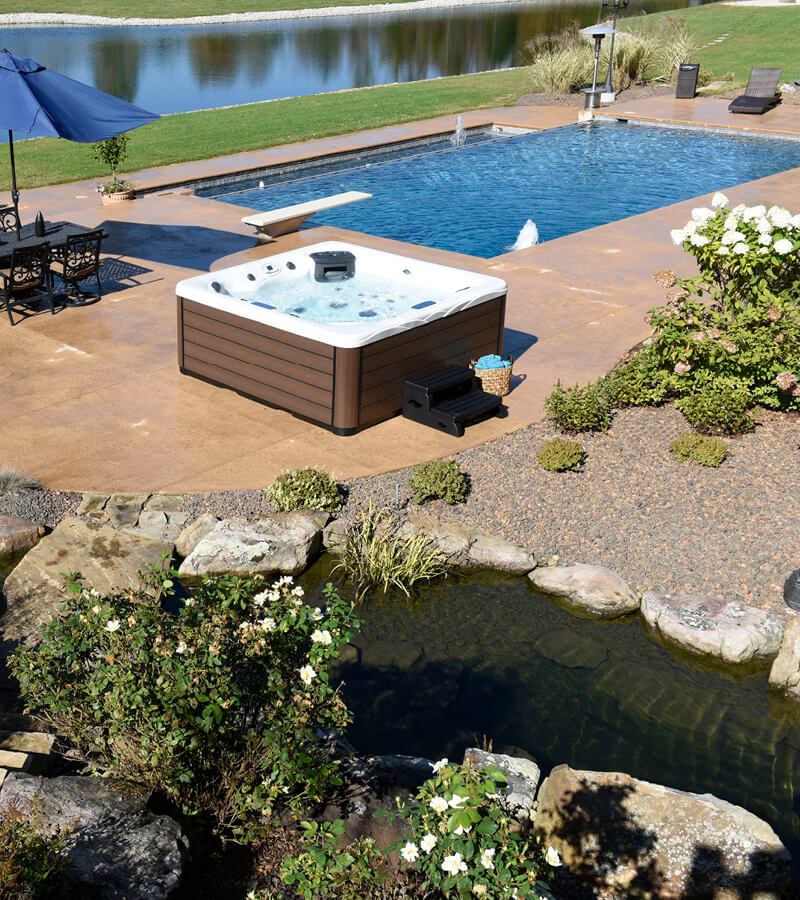 A hot tub on a landscaped patio beside a swimming pool and home