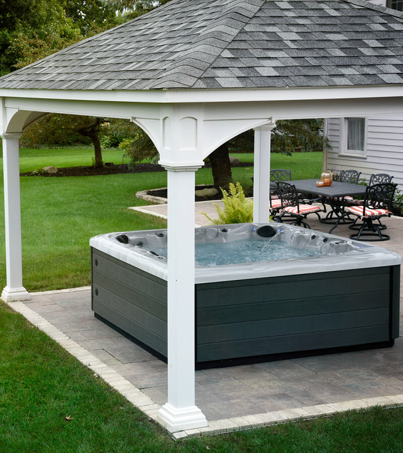 A hot tub sheltered by a white gazebo beside a green lawn